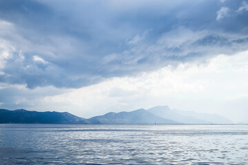 Dark clouds in the open sea. On the horizon are mountains on an island. - 412921319