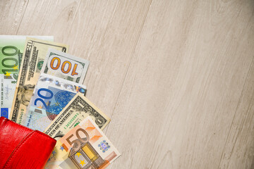 Euro and Dollar banknotes under a red wallet. Wood background