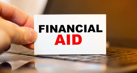 Man holding paper with FINANCIAL AID on background of office computer