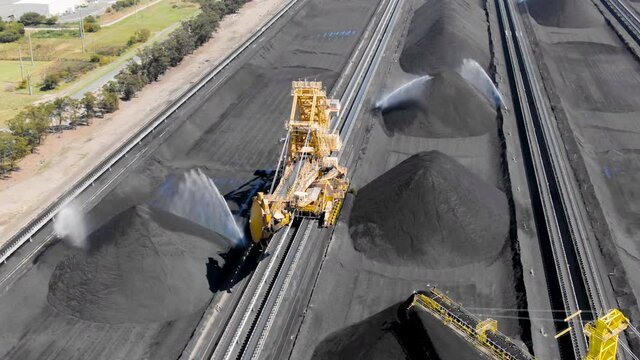 Aerial footage of coal stockpiles and bucket wheel excavators at export depot. Fossil fuel reliance, sustainability and global warming concepts.