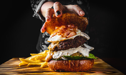 Chefs woman hand open burger with beaf steak vegetables and french fries
