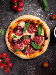 Flat lay of freshly baked pizza with olives and basil on a black background