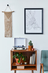 Retro composition of living room interior with mock up poster map, wooden shelf, book, macrame, armchair, plant, cacti, vinyl recorder and personal accessories in stylish home decor.