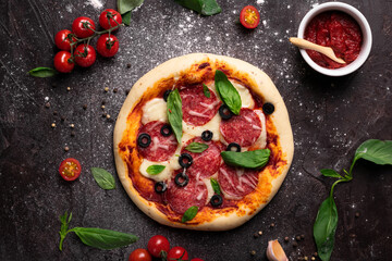 Flat lay of freshly baked pizza with olives and basil on a black background