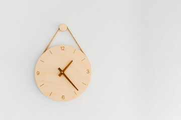 A wooden clock on a white cement wall