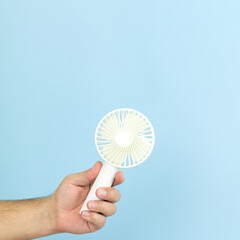 Man holding small portable usb fan close-up isolated on blue background