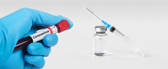 Hand holding viol with Coronavirus 2019-nCoV Blood Sample. Medical syringe and a bollte with vaccine on the background.
