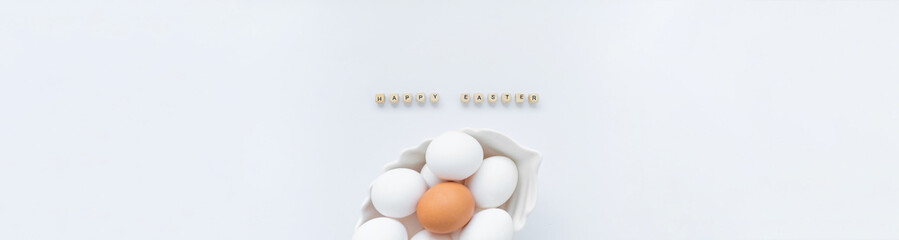 Banner with white eggs and one brown egg in a white dish and the inscription Happy Easter on a light background. Copy space, top view