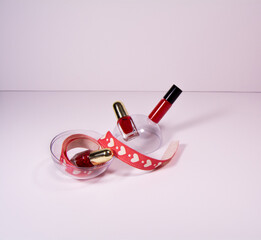 Valentine's Day background. Red lipstick and nail polish on a white background. Ribbon with hearts lies in a round shape.