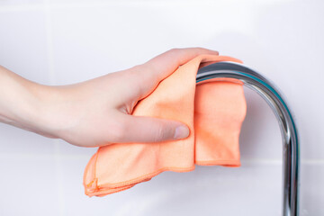The hand wipes the faucet with a napkin. Close-up in light colors. House cleaning. Cleanliness....