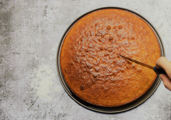 Homemade sponge cake, part of the ingredients and utensils. Cutting a portion. On a stone base and zenith view.