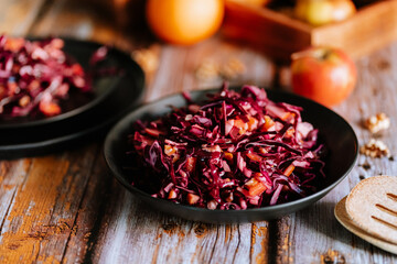 Red cabbage salad (coleslaw) with apples, oranges and walnuts on a dark wooden background, food...