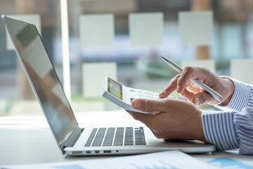Close up Business man using calculator and laptop for do math finance on wooden desk, tax, accounting, statistics and analytical research concept