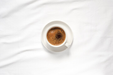 Hot coffee cup on white bedspread