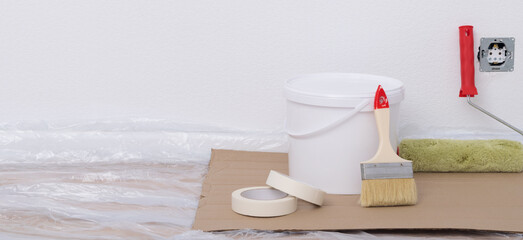 against the background of the prepared wall and floor, under painting there is a bucket and rollers for applying a protective layer on wallpaper, paints of different colors
