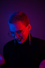 Close-up portrait of young blonde woman with short hair wearing glasses in neon light