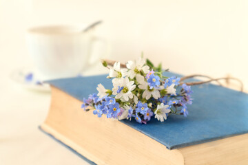 Obraz na płótnie Canvas Closed book with a bouquet of wild flowers on the background of a cup of tea, side view