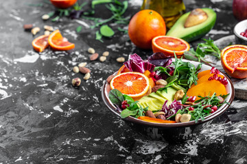 Fototapeta na wymiar Vegan, detox Buddha bowl avocado, persimmon, blood orange, nuts, spinach, arugula and pomegranate. healthy and balanced food, top view