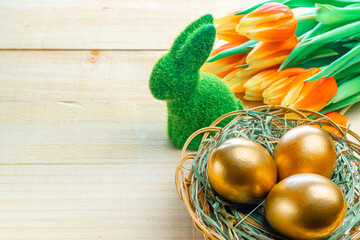 Golden easter colour eggs in basket with spring tulips, white feathers on wooden background in Happy Easter decoration. Spring holiday concept.