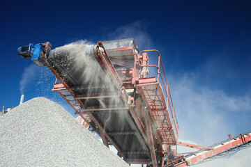 Conveyor belt of a working mobile crusher machine, close-up, with blown away by the wind white...
