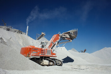 Mining excavator for loading rubble up with lifted bucket on a background of the dark blue sky.