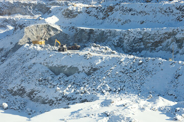 Heavy mining machinery works in a snow-covered stone quarry.