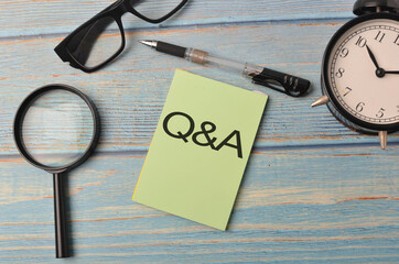 Top view of a magnifying, pen, alarm clock and spectacles with text Q&A on wooden background.Selective focus.