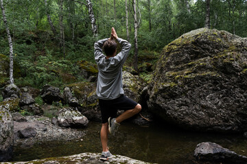 young man stands in the forest. look from the back. outdoor yoga exercises