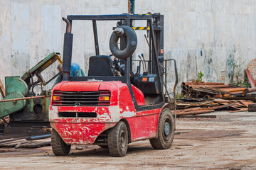 Fototapeta na wymiar Diesel red battered forklift truck on the street against the background of scrap metal
