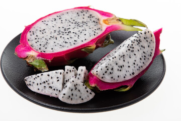 Ripe dragon fruit or pitaya cut in half with seeds visible on black plate