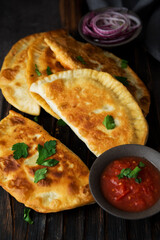 Homemade fried empanadas with pork, chebureks with mushrooms on a wooden board.