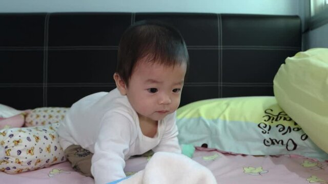 portrait of 8 month Asian Chinese baby boy looks and move around surprisely on a bed