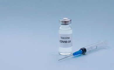 Syringe and COVID-19 vaccine on light blue background, copy space. Coronavirus vaccination and...