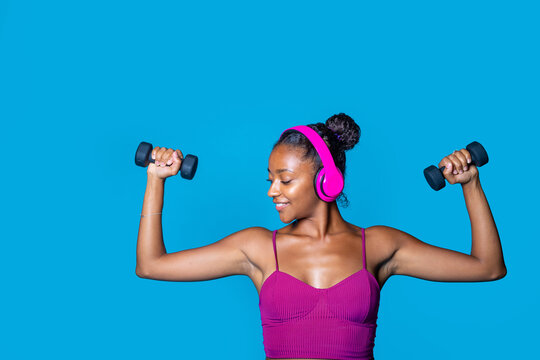 Fit young black woman weight lifting on blue background doing workout
