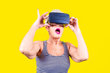 Eldelry woman on yellow background using vr glasses - Isolated caucasian old woman wearing futuristic headset