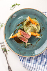 sliced venison fillet steak with mashed potato and vegetables on blue plate