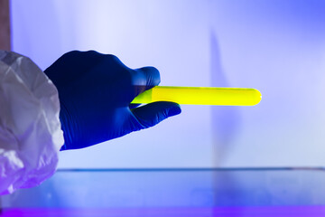Fluorescein glowing in flask under ultraviolet light. A closeup of man hand holding up a vial  fluorescent liquid.
