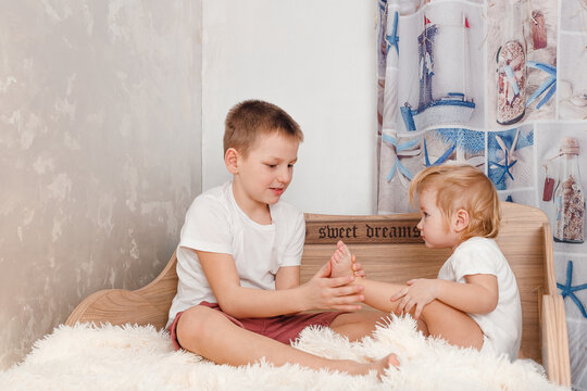 Older brother tickles younger sister's bare feet on bed at home