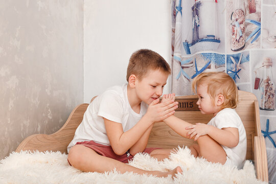 Older brother tickles younger sister's bare feet on bed at home