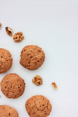 Fototapeta na wymiar Homemade oatmeal cookies with walnuts on white table. Overhead view of oat biscuits and nuts on white background with copy space