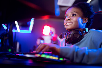 Young african happy woman professional gamer win in online video game with headphones, neon...
