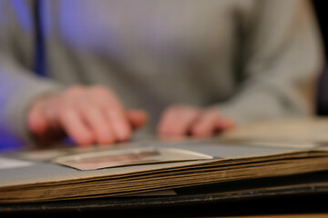 Elderly woman looks through an family album with old photos at table at home. Old granny memories past times and remembering his life.