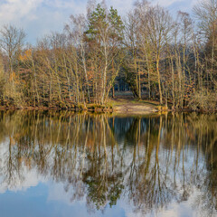 Dal van de Roodebeek, Dutch nature reserve with a lake with mirror reflection on the water surface of the surrounding bare trees, sunny winter day in Schinveld, South Limburg in the Netherlands