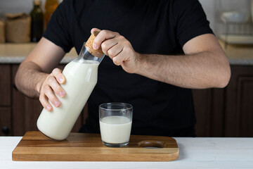 A man opens a bottle of fresh milk at home in the kitchen Breakfast happy family, father with food