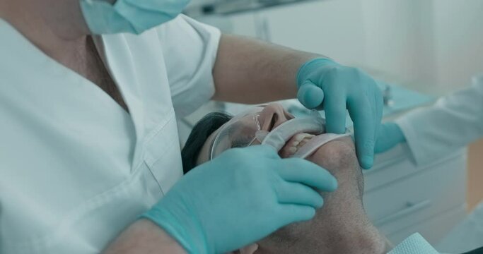 During dentist`s appointment male Arabian patient is having his gum examined by dentist. Patient is having cheek retractor and protective eyeswear on him.