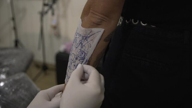 Crop tattoo master applying sketch on arm of client