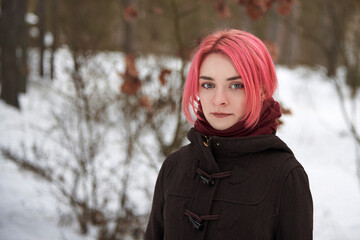 Portrait of a young woman with bright pink hair in the winter in the forest.