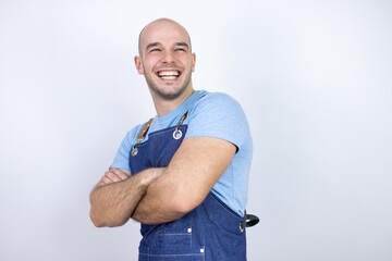 Young bald man wearing apron uniform over isolated white background with a happy face standing and smiling with a confident smile showing teeth with arms crossed