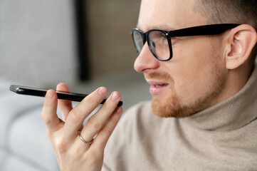 A confident guy is recording voice message, a young man is using voice assistant on the smartphone....