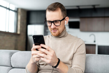 Obraz na płótnie Canvas Handsome guy is using smartphone for messaging, texting, a young man in smart casual wear sitting with a phone in the hands, typing a message, chatting in the networks